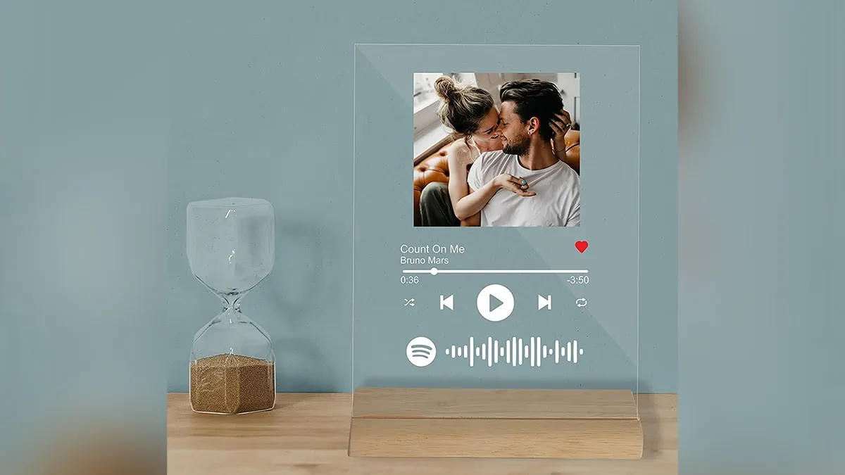 On a table next to an hourglass is a piece of personalized glass art with a couple's photograph and a song dedicated to them.