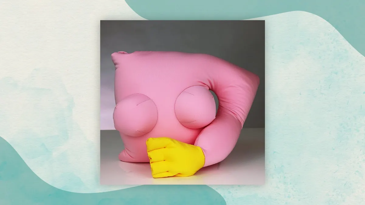 A girlfriend pillow with a pink colored body and a yellow colored hand kept on a white table as one of the special gift for long distance relationships. 