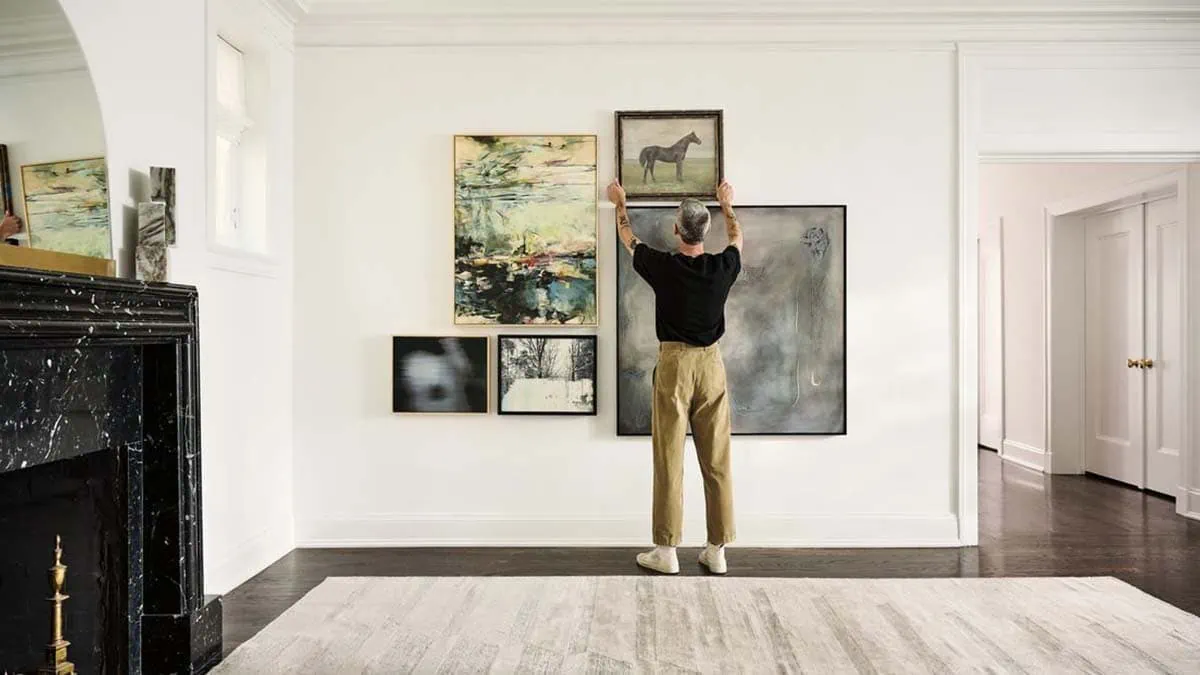 a man hanging a painting with proper wall spacing